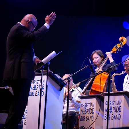 Christian McBride conducting in front of Kanoa Mendenhall on bass and big band members on stage for MJF 62
