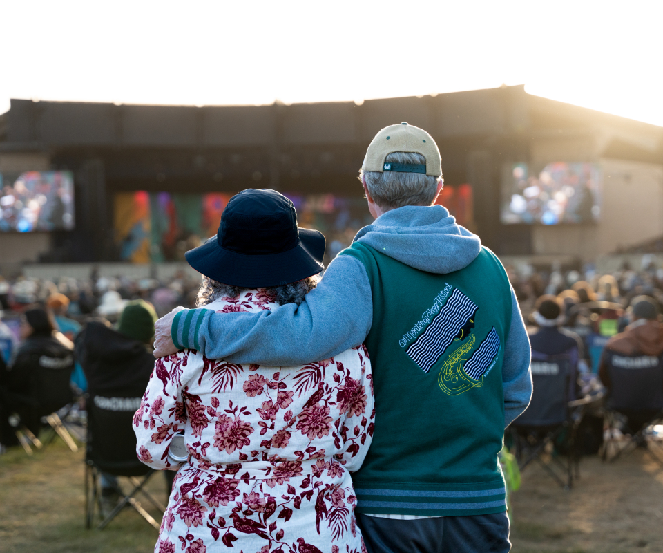 Back of two guests looking at a stage behind the out of focus audience in lawn chairs.