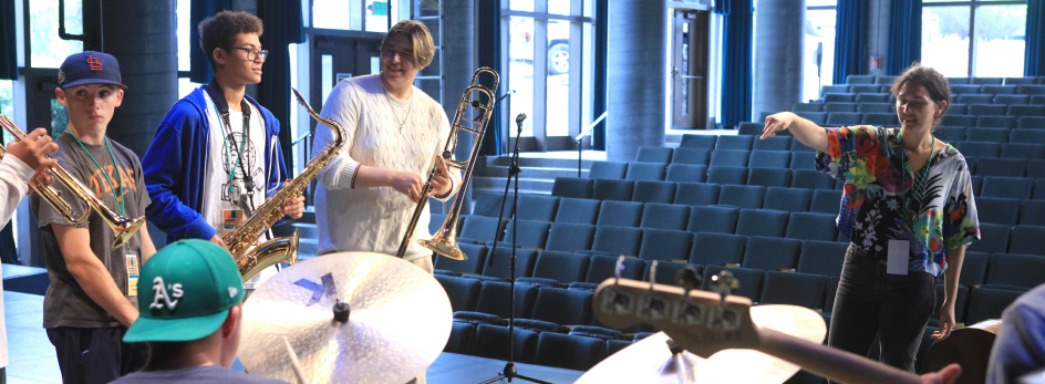 Students with their instruments and an instructor leading them in an auditorium