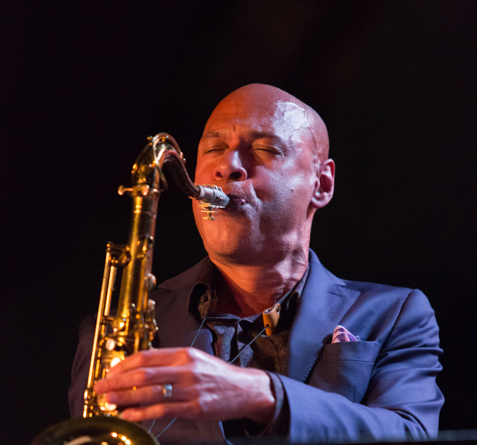 Joshua Redman performing with his saxophone in front of a black background