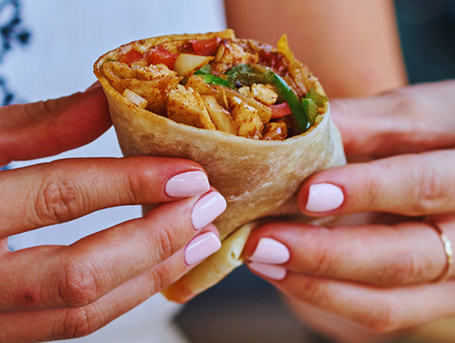 Hands holding half of a burrito filled with chicken and vegetables