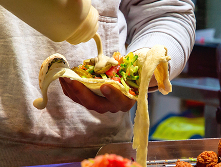 Someone putting a sauce on top of an open face wrap with vegetables