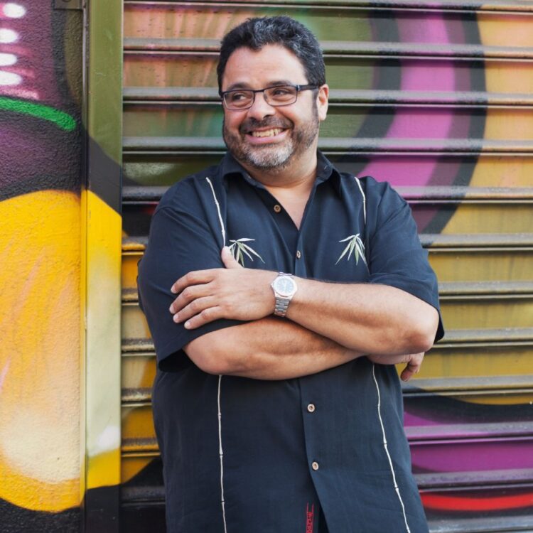 Arturo O'Farrill leaning against a bright spray painted wall