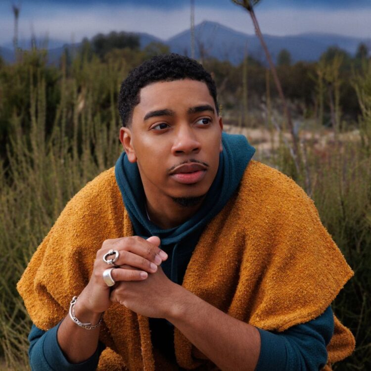 Christian Sands sitting in a field with tall grass