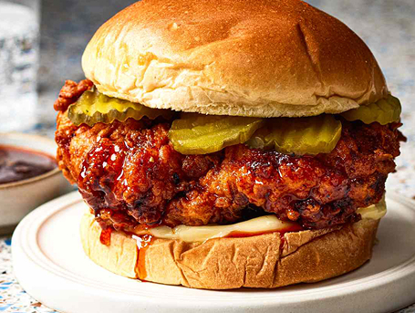 A sauced chicken sandwhich with pickles on a plate