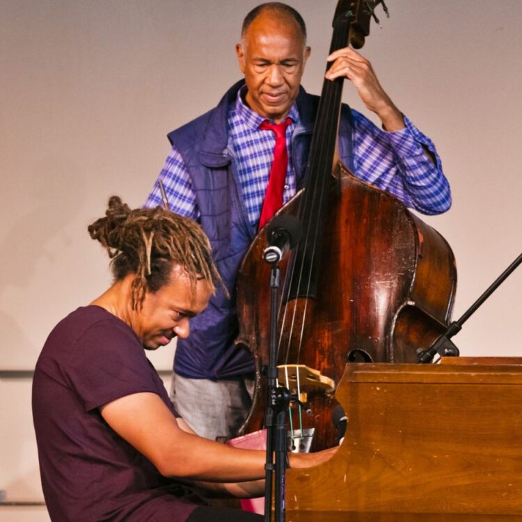 John Clayton performing with his bass behind Gerald Clayton performing on a piano