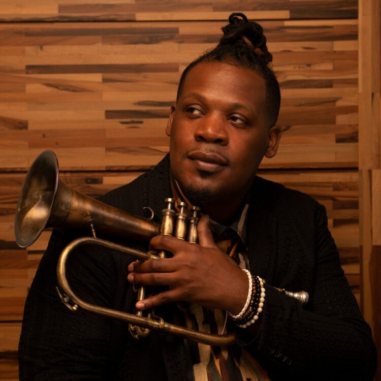 Keyon Harrold holding a trumpet in front of a wooden wall