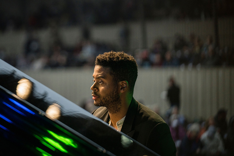 Chris bowers facing an open piano with an out of focus audience behind him