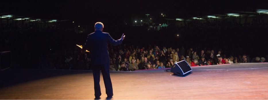 Back of a man on a stage, speaking to an audience