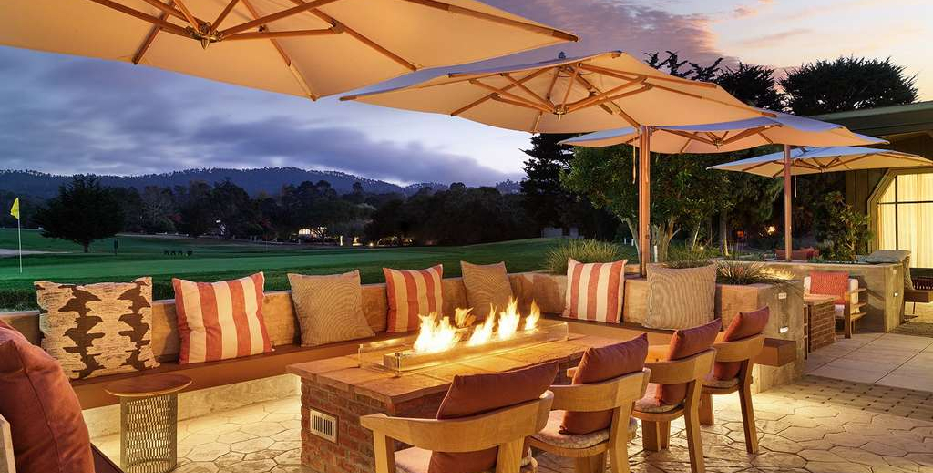 Outside dining area in front of a golf course. Benches and chairs around brick tables with umbrellas above