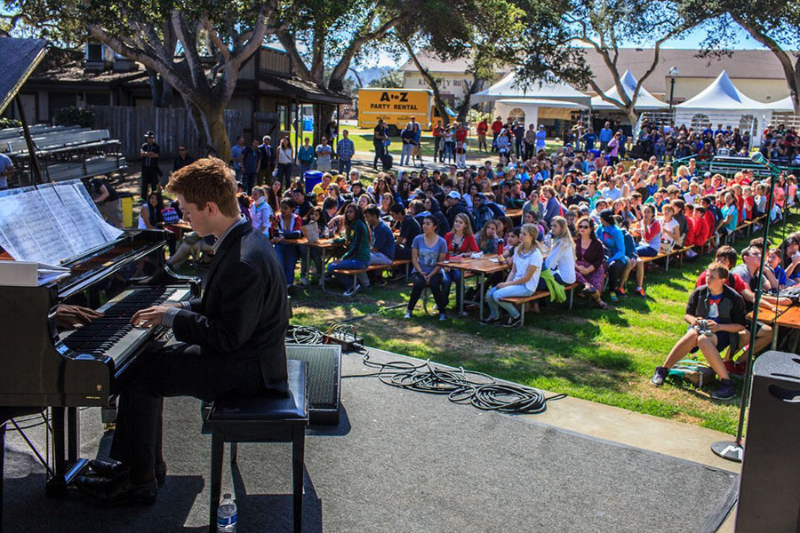 Man playing piano outside on a stage in front of an audience