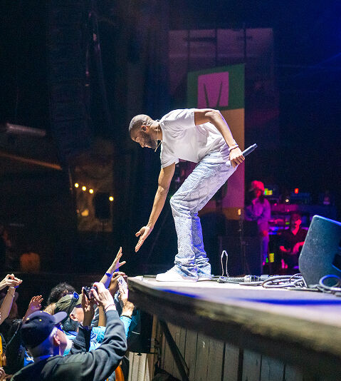 Trombone Shorty on stage reaching a hand out to an audience member