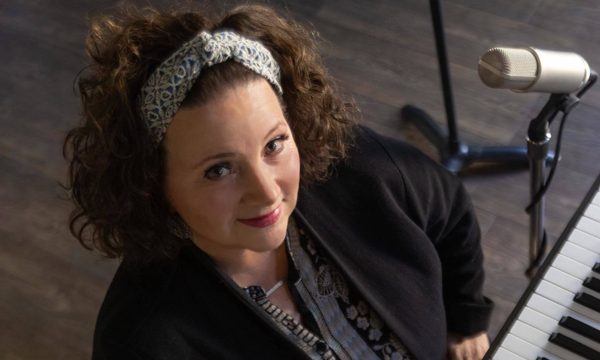 A white woman with brown curly hair sitting in front of a piano