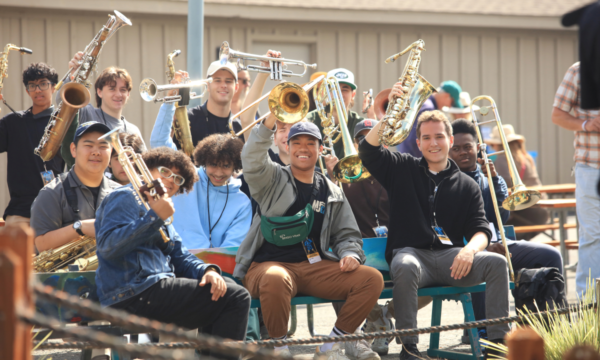 A group of student musicians waving at the camera holding their trumpets, saxophones and trombones in the air